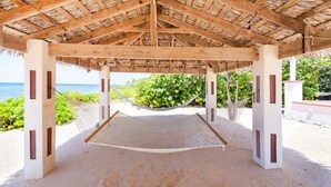 A beach cabana with a thatched roof, a hammock, and a view of the ocean.