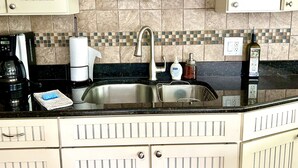 Una cocina con un lavamanos de acero inoxidable, una cafetera y una botella de vinagre orgánico.