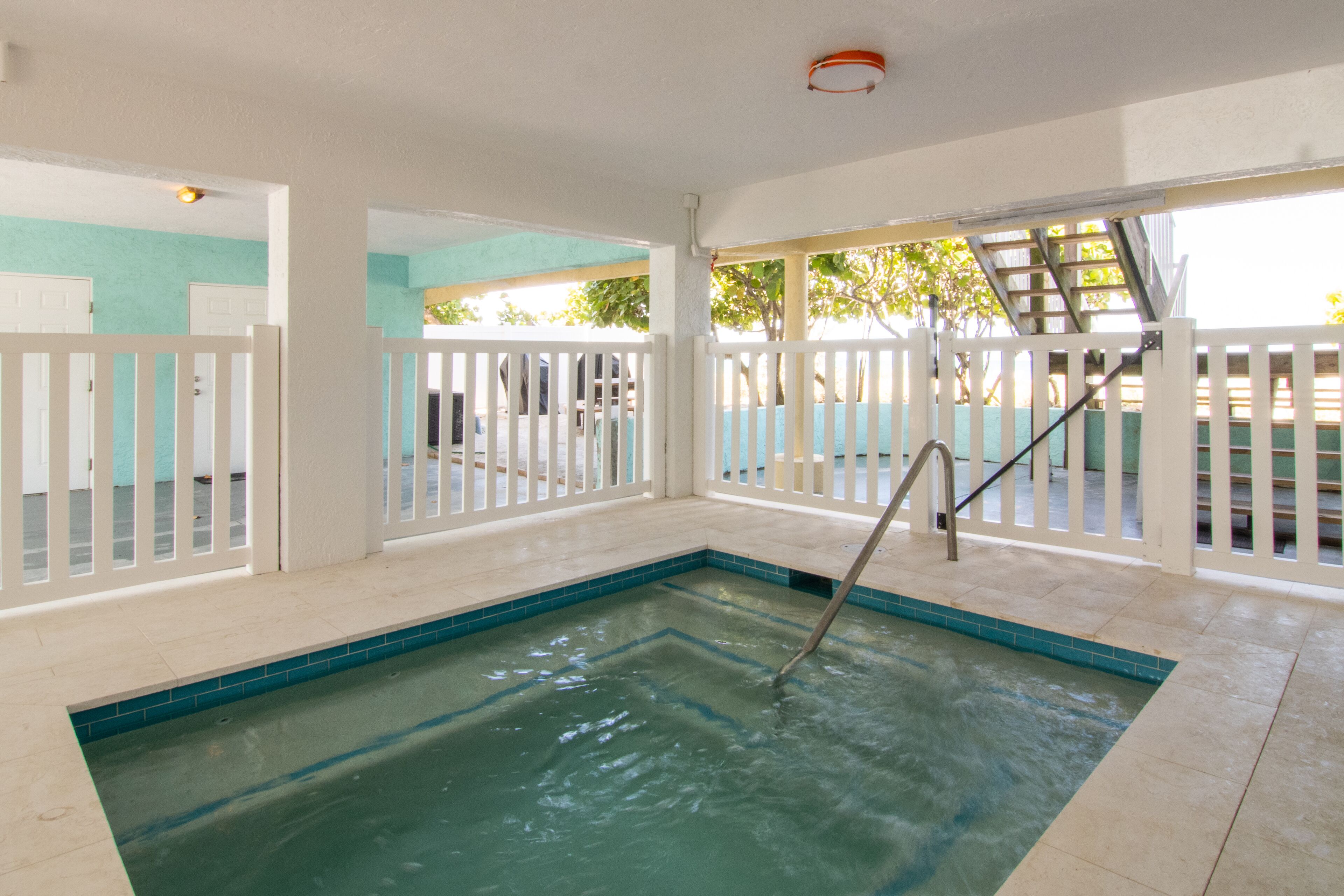 A swimming pool with a ladder, surrounded by white railings and a tiled floor.