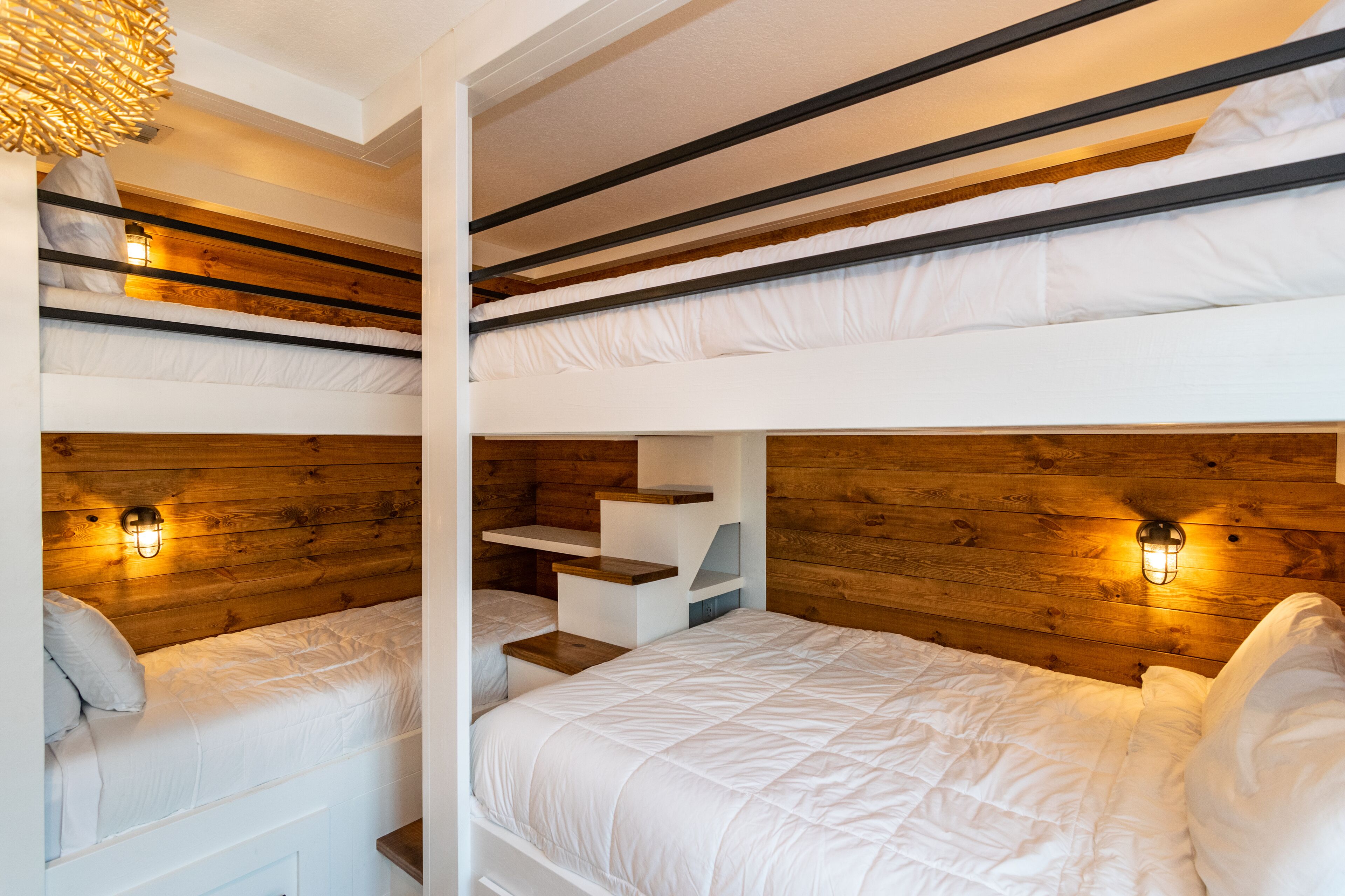 A bunk bed room with wooden headboards and wall-mounted lighting.