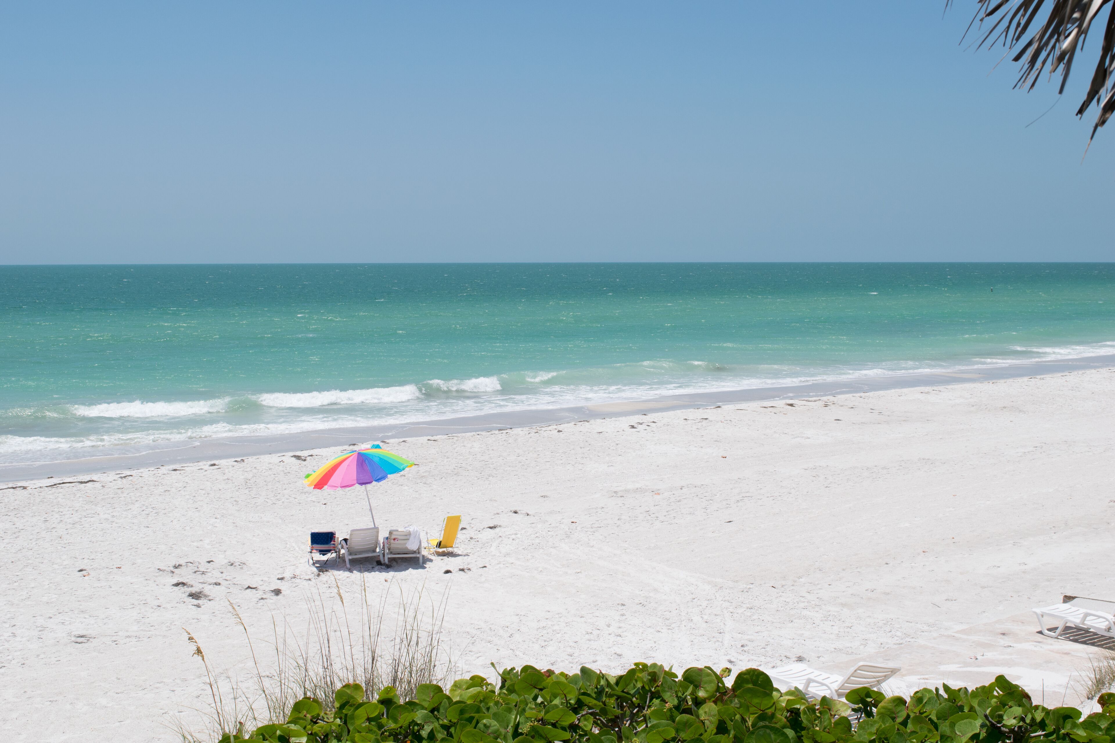 A beach with a colorful umbrella, a beach chair, and a lounge chair.