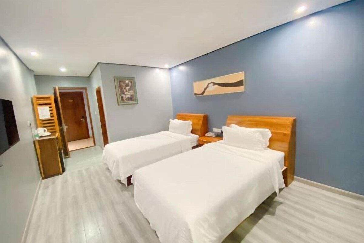 A hotel room with two beds, a wooden nightstand, a desk with a chair, and a door leading to another room.