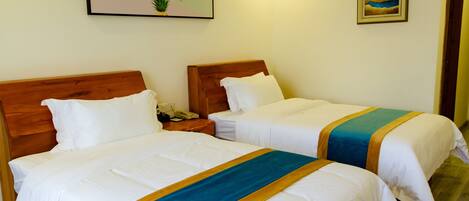 Two single beds with wooden headboards, white bedding, and a blue and gold striped runner.