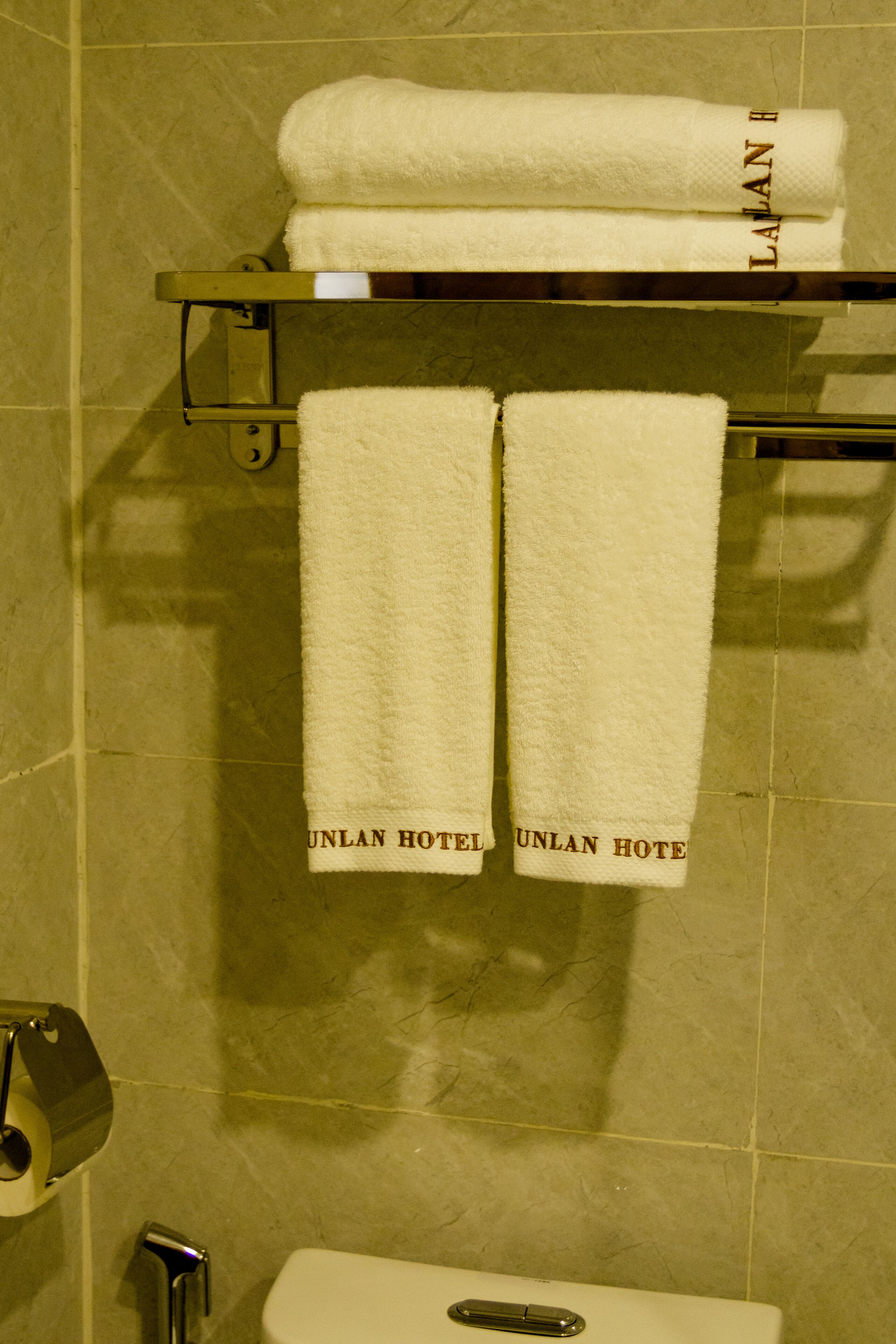 A bathroom with a toilet, a towel rack with two towels, and a roll of toilet paper.