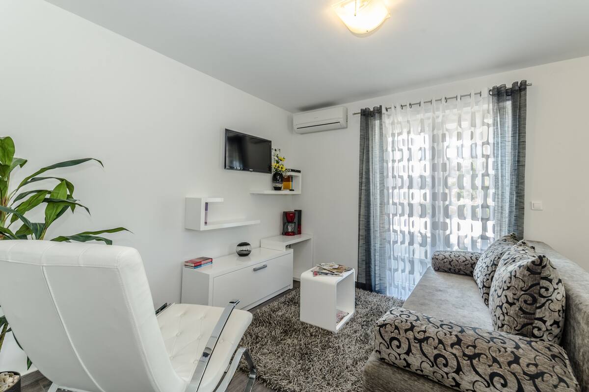 Un salon moderne avec un canapé blanc, un fauteuil blanc, une petite table d’appoint blanche, un téléviseur fixé au mur et une plante en pot.
