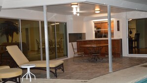 Un espace extérieur abrité comprenant une piscine, des chaises longues, une table à manger et un coin cuisine.