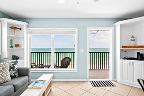A room with a view of the beach, a grey sofa, a small table with a tray, and a cabinet with a sign.