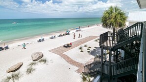 Une vue sur la plage avec un escalier menant à un balcon, des chaises longues et un palmier.