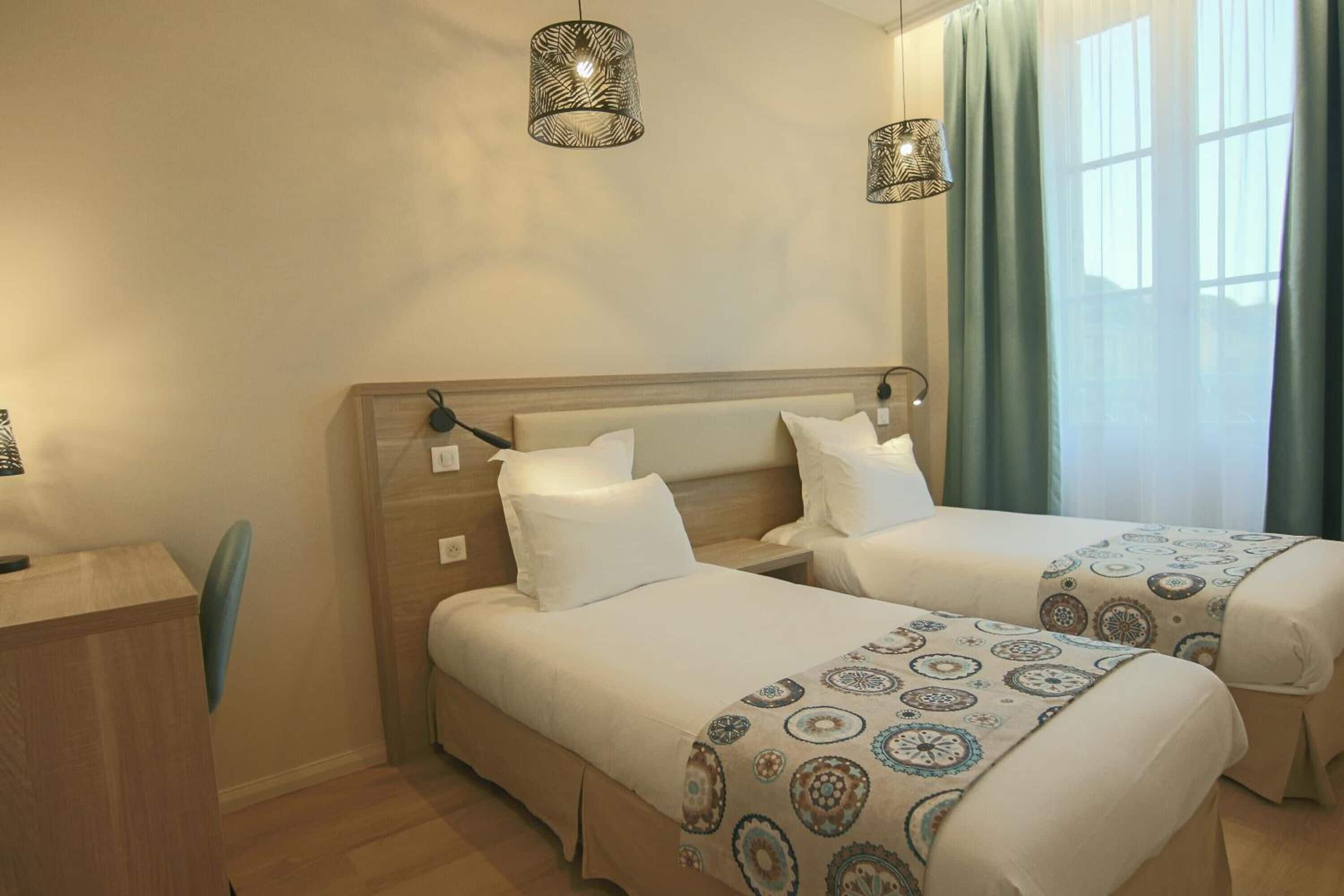 A hotel room with two beds, a desk, and a window with curtains.