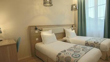 A hotel room with two beds, a desk, and a window with curtains.