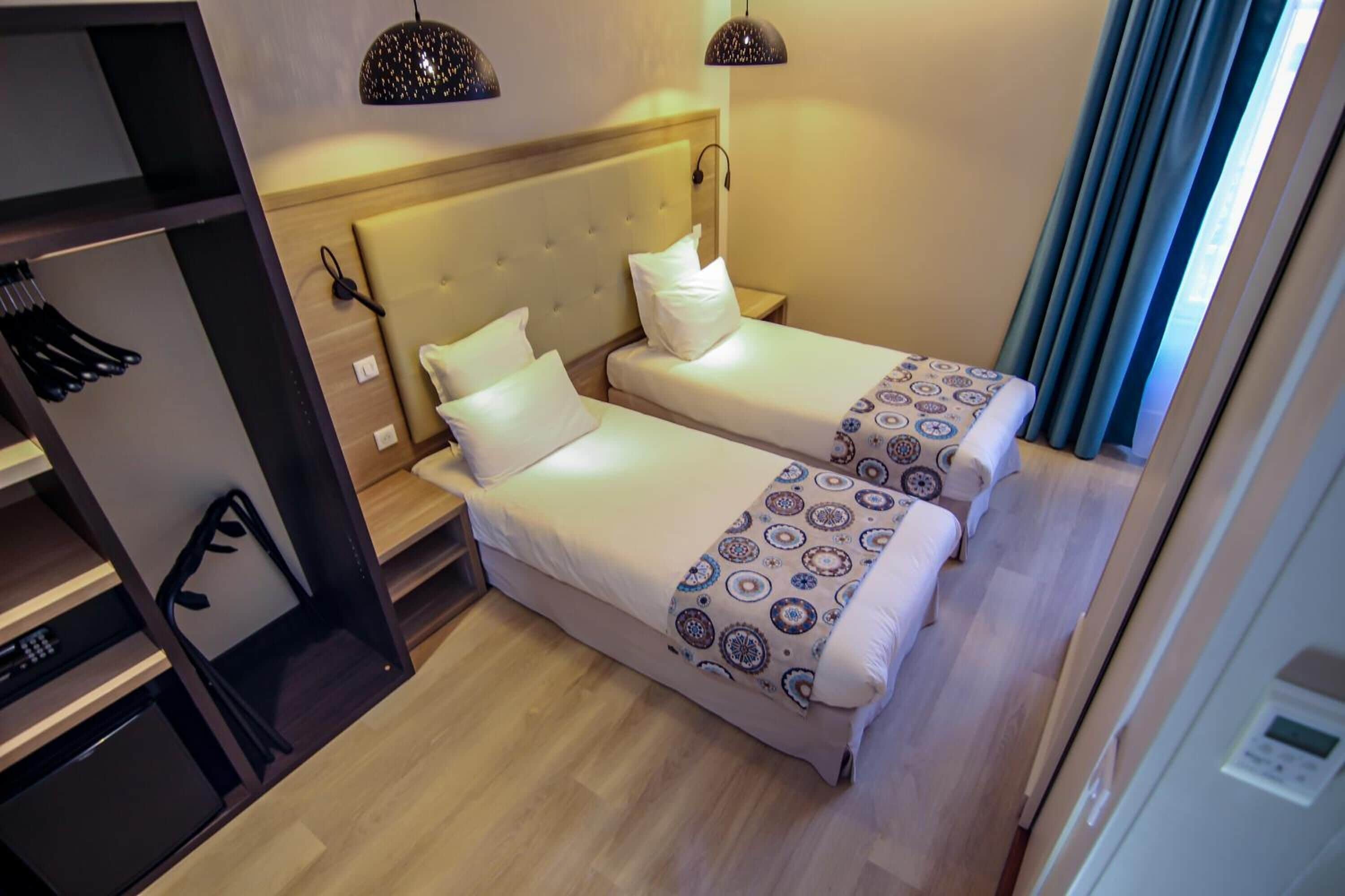 Une chambre d’hôtel avec deux lits simples, une armoire et un bureau avec une chaise.