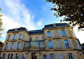 Ein historisches Gebäude mit Schildern, auf denen "HOTEL" und "MONTAIGNE" stehen, mit klassischer Architektur, symmetrischen Fenstern und einem zentralen Eingang.