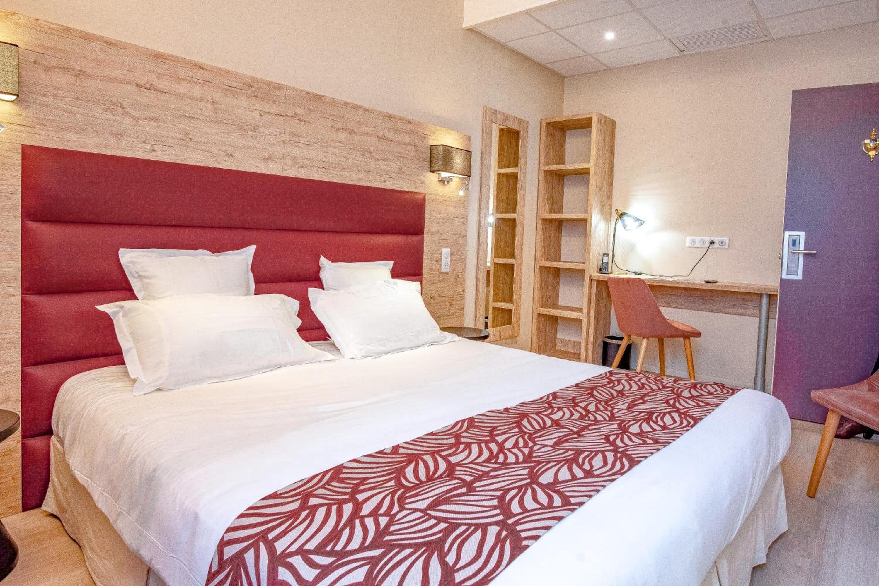 A hotel room with a large bed, a wooden headboard, a desk with a chair, and a bookshelf.