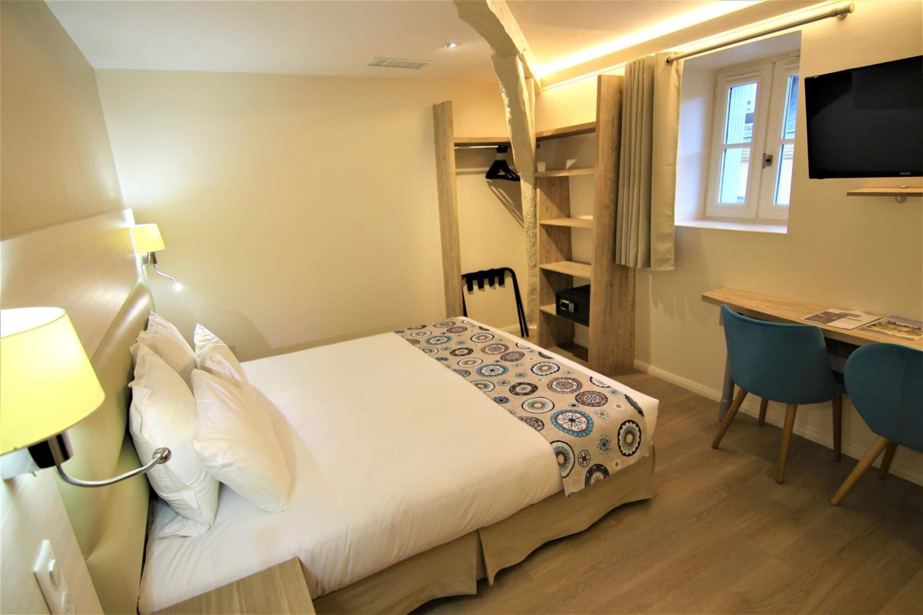A bedroom with a bed, bedside lamp, desk, chairs, and a TV.
