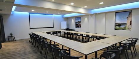 Un salón de conferencias con una larga mesa, varias sillas, una pantalla de proyector y una pizarra.