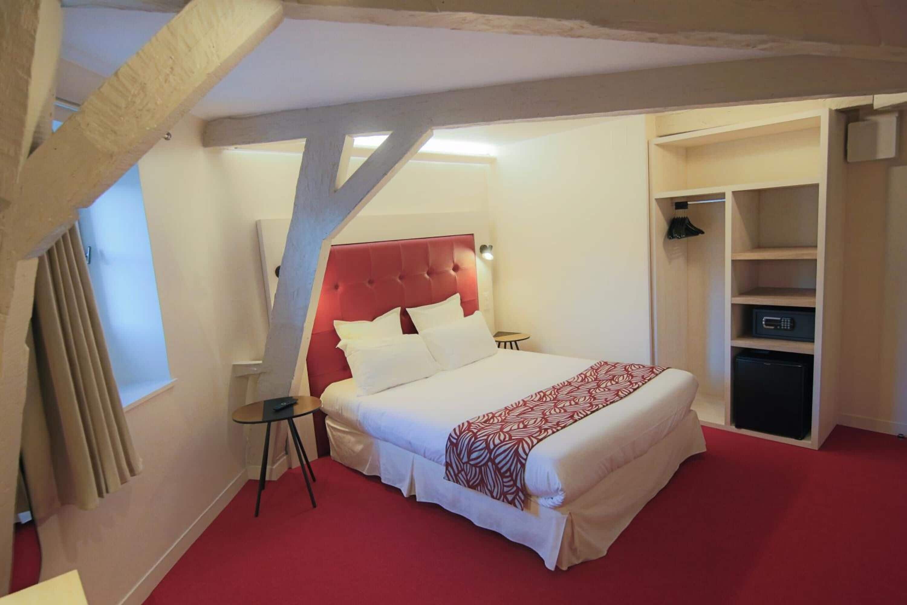 A bedroom with a red headboard, a bed with white bedding, a small table, and a closet with shelves.