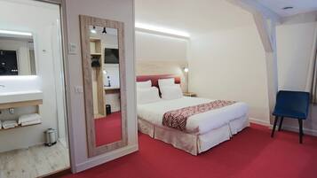 A hotel room with a bed, a chair, a mirror, and a bathroom with a sink and towel rack.