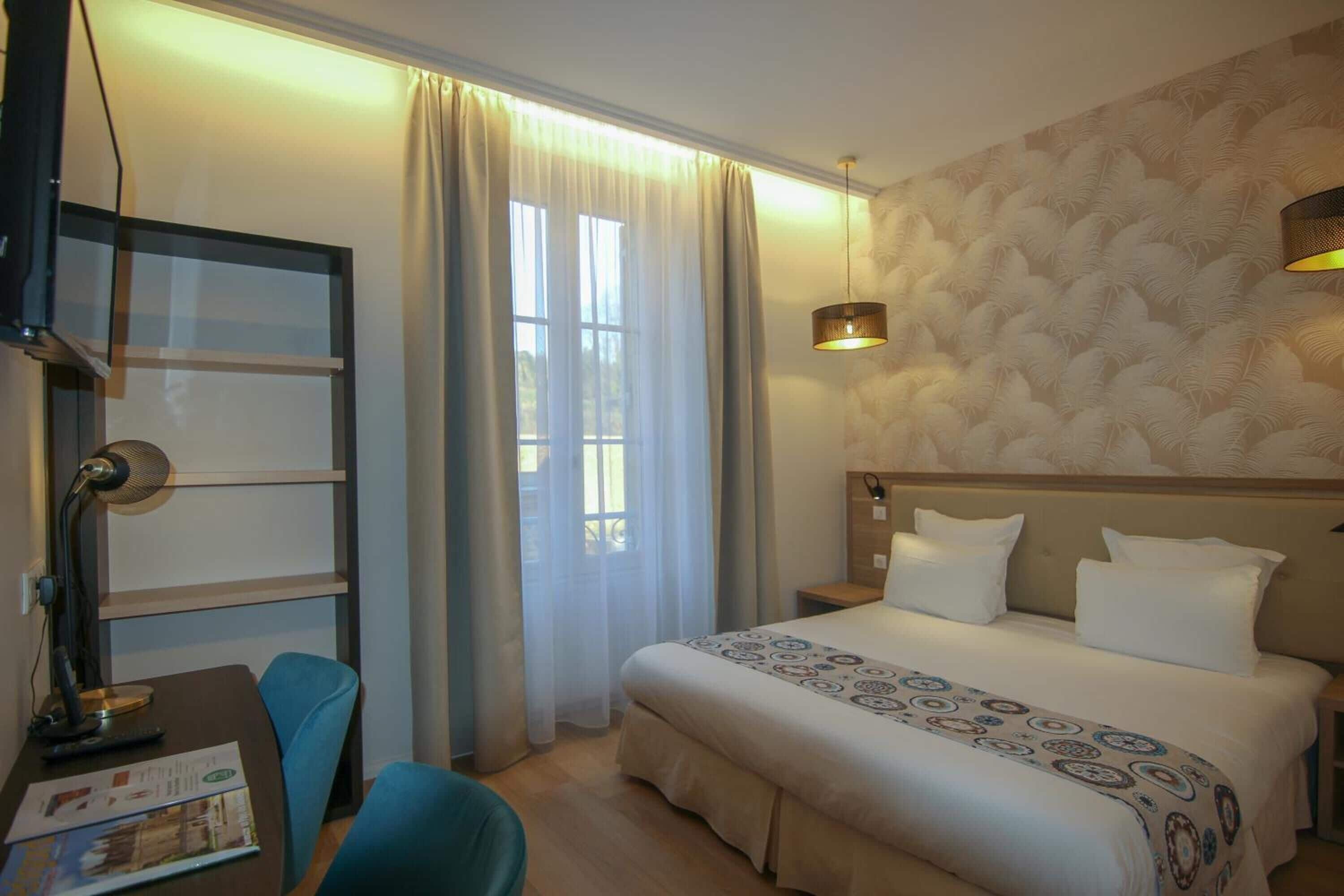 Ein Hotelzimmer mit einem Bett, einem Schreibtisch mit Lampe, einem Sessel und einem Fenster mit Vorhängen.