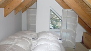 Une chambre avec un plafond en pente, une fenêtre et un lit recouvert de linge de lit blanc.