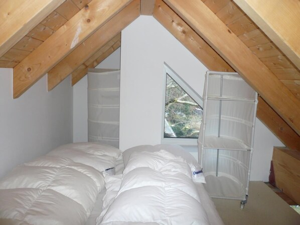 A bedroom with a sloped ceiling, a window, and a bed with white bedding. - Hookipa, App. OG #390<br>Location:<br>The apartment is located on the upper floor of a modern 2-family house and is very individually furnished. The house is in the second row in quiet Alt-Westerland.<br>Size:<br>2-room apartment approx. 4 (Westerland)