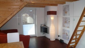 Une pièce de style loft avec un plafond en bois, un canapé rouge, une table en bois, un téléviseur et un escalier.