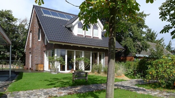 Une maison avec un toit en pente, une façade en briques et un porche à l’avant.