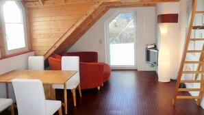 Une pièce de style loft avec un plafond en bois, une table à manger avec des chaises, un canapé rouge, une lampe blanche et une échelle.