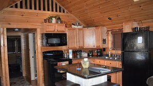 Cocina de cabaña de madera con una isla central, microondas, estufa, refrigerador y armarios de madera.