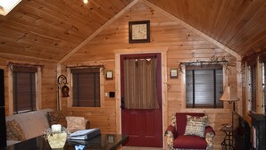 Un acogedor interior de cabaña de troncos con techo de madera, una puerta roja, un reloj, una chimenea y un comedor.