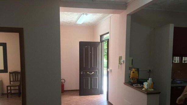 A spacious hallway with a tiled floor leading to a door, a small seating area with a chair, and a kitchenette area with a sink and countertop.