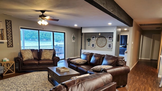 A spacious living room with two brown leather sofas, a wooden coffee table, and a large window offering a view of a deck. - LAKEFRONT PADDLEBOARD KAYAK WATERMAT SWIMMING FIREPIT GRILLING SUNDECK FISHING  (Roach)