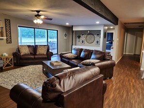 A spacious living room with two brown leather sofas, a wooden coffee table, and a large window offering a view of a deck.