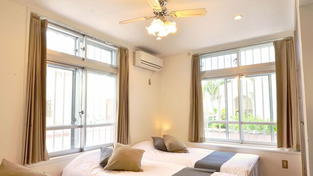 Ein Hotelzimmer mit zwei Betten, großen Fenstern, einer Klimaanlage und einem Deckenventilator.