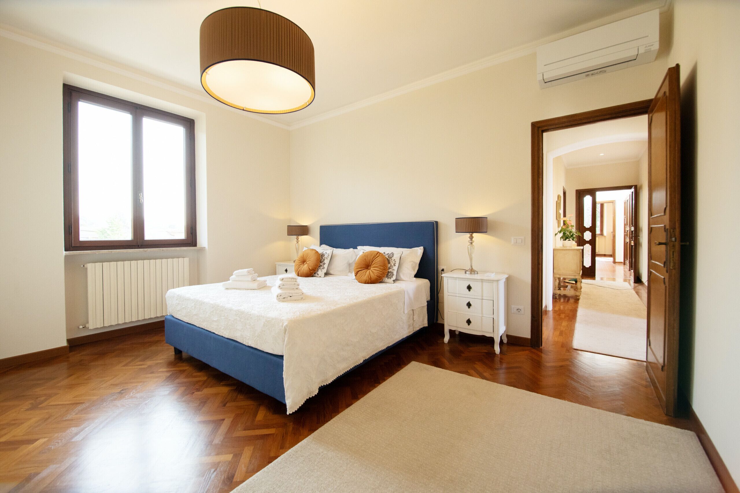 A bedroom with a bed, bedside tables, a window, and an air conditioning unit.