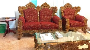 A room with two ornate red upholstered chairs with gold detailing, a glass coffee table, and a small wooden side table with a green basket. - Maya Service Apt (Dhaka)