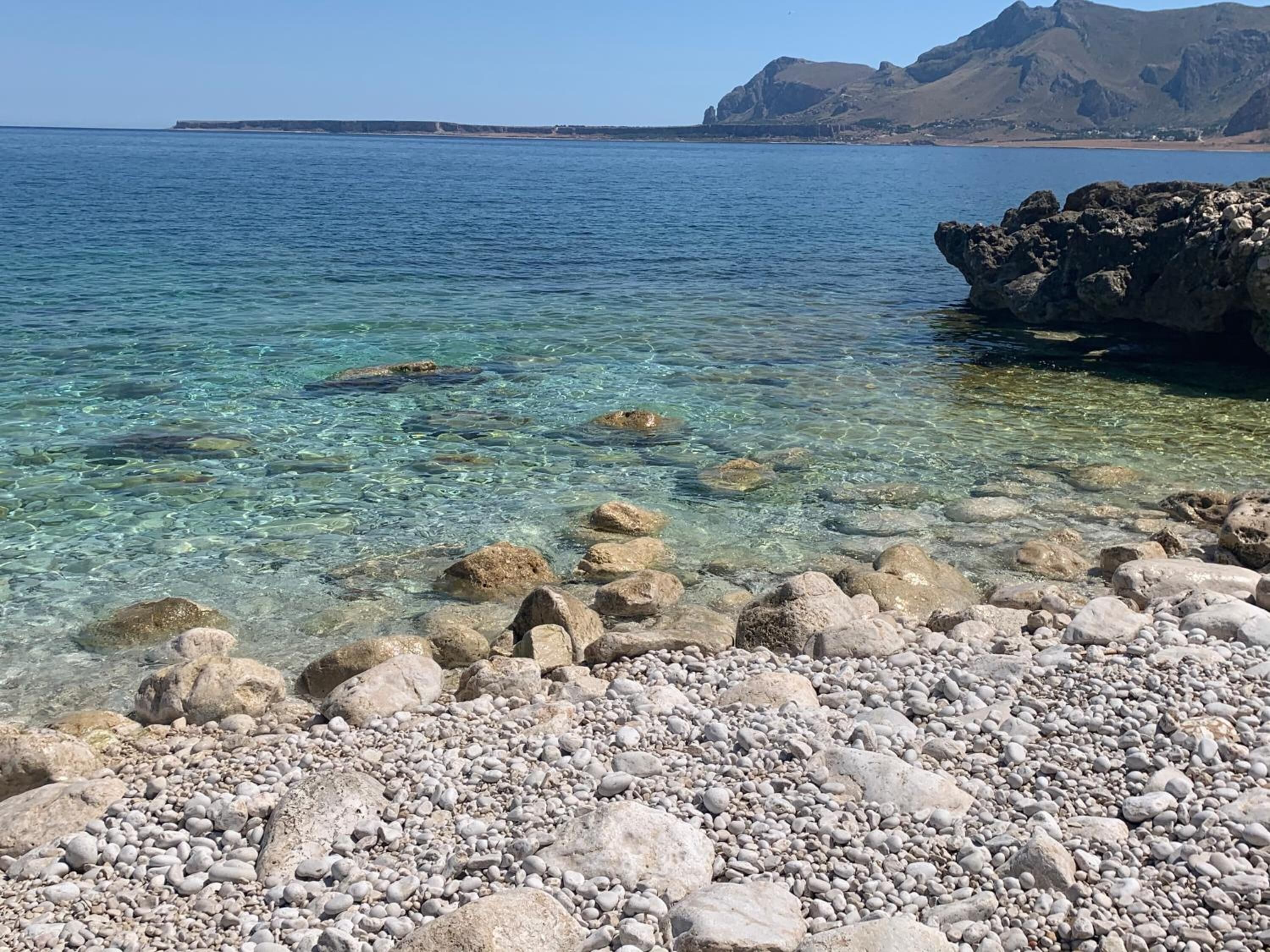 Una costa rocosa con agua cristalina y montañas a la distancia.