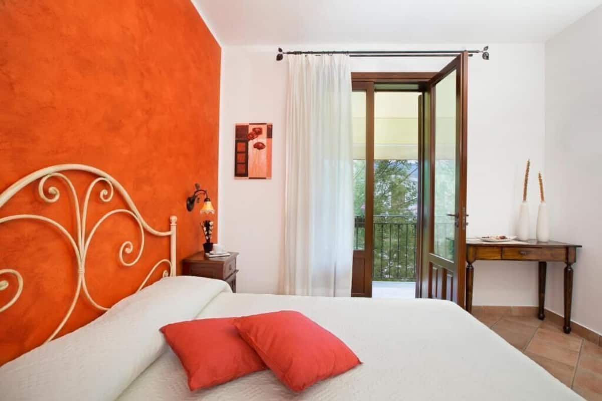 Une chambre à coucher comprenant un lit, une table de chevet, une lampe, une fenêtre avec des rideaux et une vue sur un balcon.