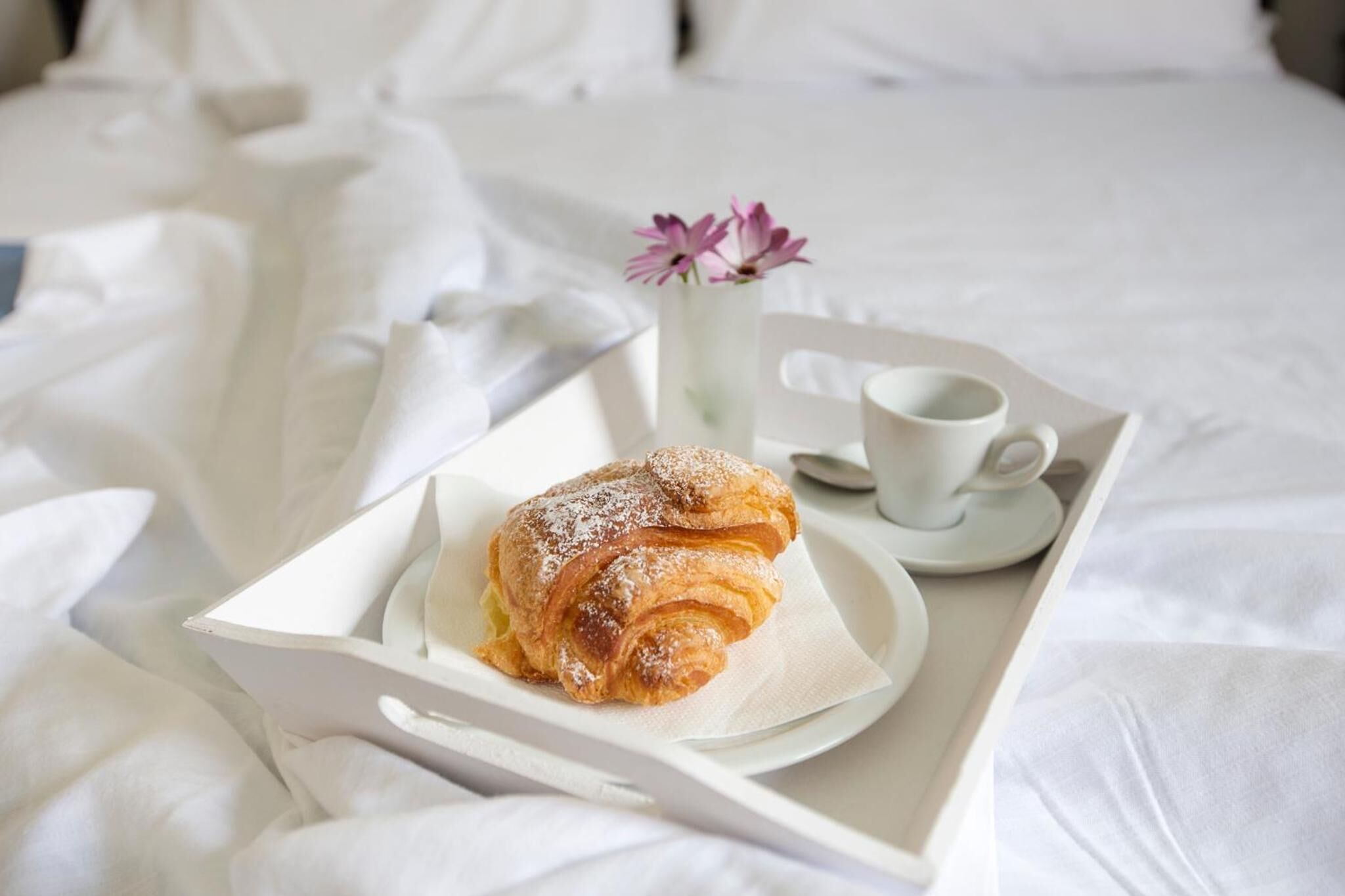 Una bandeja con un pastel y una taza de café sobre una cama con sábanas blancas.
