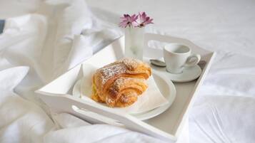 Una bandeja con un pastel y una taza de café sobre una cama con sábanas blancas.