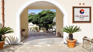 An entrance to Cala di Ponente Hotel with an arched doorway, potted plants, and a signboard. - Cala di Ponente (San Vito Lo Capo)