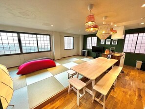 Habitació amb esteigs de tatami, taula de fusta, bancs, coixí vermell i televisió.
