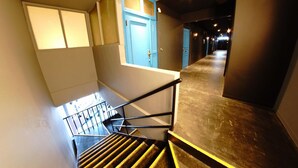 A staircase with a handrail, a blue door, and a corridor with lights. - Swiss Inn (Sapporo)