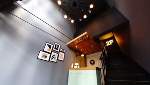 A reception area with a wooden counter, framed pictures on the wall, and a staircase leading to the second floor. - Swiss Inn (Sapporo)