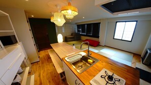 A modern kitchen with a wooden countertop, stainless steel sink, and a gas stove. There is a window providing natural light and a red cushion on the floor. - Swiss Inn (Sapporo)
