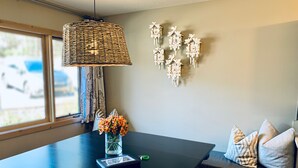 Un espace repas moderne avec une table en bois foncé, un luminaire suspendu en osier, un vase de fleurs et des horloges à coucou fixées au mur.