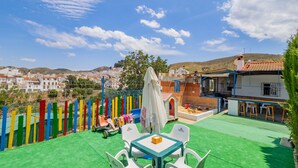 Eine Terrasse mit grünem Kunstrasen, einem Tisch mit Stühlen und Blick auf eine Stadt im Hintergrund.