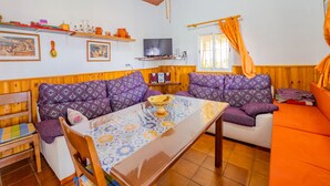 Ein gemütliches Wohnzimmer mit Holzboden, einem Fernseher, einem Tisch mit gemustertem Tischläufer und zwei Sofas mit gemusterten Kissen.