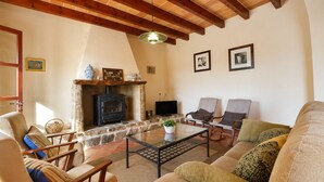 Una sala de estar acogedora con chimenea de piedra, vigas de madera en el techo, asientos cómodos y un televisor.