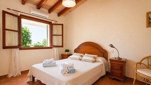 Un dormitorio con cama, mesita de noche, lámpara, silla y ventana con cortinas.