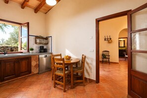 A kitchen with a dining table, chairs, a dishwasher, and a window overlooking a garden. - Charming House - 6 pax, - Wifi Free - Sat TV - Private Salat Pool (Manacor)